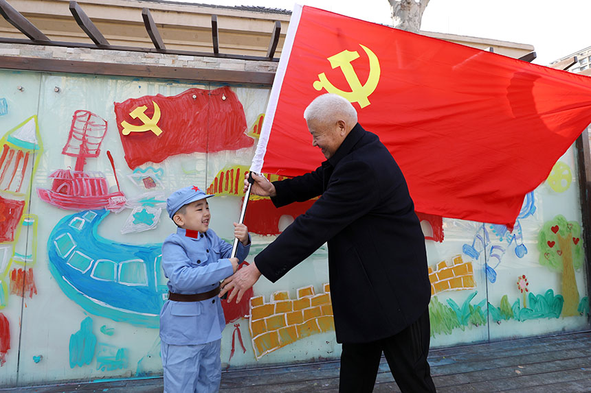 老党员爷爷将党旗庄重的传递给给小朋友。刘祺摄