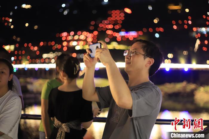 游客吹着夜晚徐徐的江风，欣赏龚滩古镇万千灯火的夜景。　马佳欣 摄